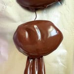 Two oval-shaped crunchy peanut butter eggs coated in melted chocolate rest on a sheet of foil, with excess chocolate dripping downward.