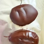 Four oval-shaped pieces of crunchy peanut butter eggs, coated in chocolate, are arranged in a vertical line on a sheet of foil.