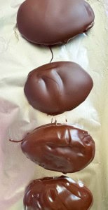 Four oval-shaped pieces of crunchy peanut butter eggs, coated in chocolate, are arranged in a vertical line on a sheet of foil.