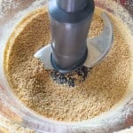 Ground crumbs and crunchy peanut butter eggs in a food processor with a metal blade attachment, showing a coarse, sandy texture.