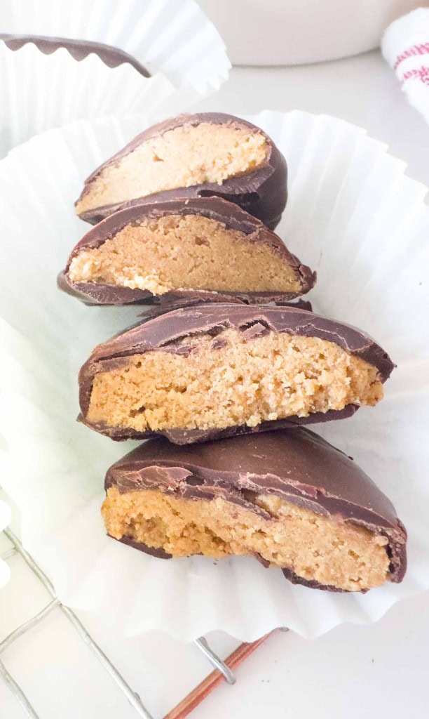 Four crunchy peanut butter eggs are cut in half and stacked on a white paper liner, showing their creamy, golden filling.