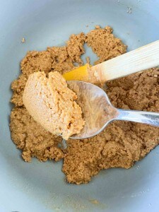 Spoon holding a scoop of crunchy peanut butter cookie dough above a mixing bowl, with a spatula resting on the side—perfect for making delicious peanut butter eggs.
