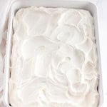 A rectangular white baking dish filled with Heath Bar Poke Cake, topped with a thick, swirled layer of whipped cream.