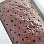 A Heath Bar Poke Cake baked in a white rectangular pan with evenly spaced holes poked across the chocolatey surface.