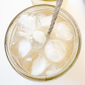 A glass filled with round ice cubes and a light-colored Mocktail Moscow mule, served with a metal straw inside.