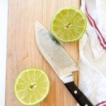 A halved lime and a chef's knife rest on a wooden cutting board next to a white towel with red stripes—perfect prep for a refreshing Mocktail Moscow mule.