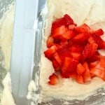 Chopped strawberries on top of creamy white batter in a mixing bowl.
