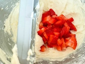 Chopped strawberries on top of creamy white batter in a mixing bowl.