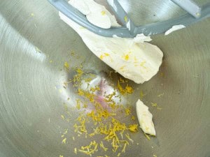 Cream cheese and lemon zest in a metal mixing bowl with a mixer paddle attachment.