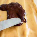 A knife spreads melted chocolate over a smooth layer of peanut butter mixture.
