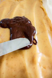 A knife spreads melted chocolate over a smooth layer of peanut butter mixture.