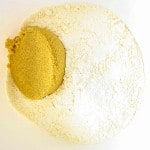 A white bowl containing a mound of flour and a scoop of brown sugar placed next to each other.