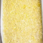 Rectangular baking pan lined with parchment paper, filled with a flat, uncooked mixture of oats and butter, pressed evenly across the surface.