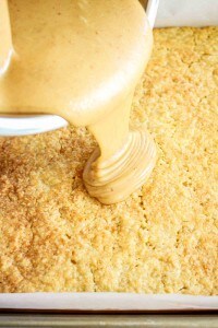 Golden cake base with creamy peanut butter frosting being poured on top.