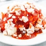 A plate of food featuring chopped imitation crab meat and red sauce poured over a mound of cream cheese.