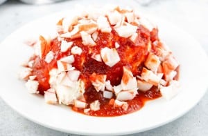 A plate of food featuring chopped imitation crab meat and red sauce poured over a mound of cream cheese.