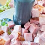 Cubed ham in a food processor bowl with chopped celery and onions.