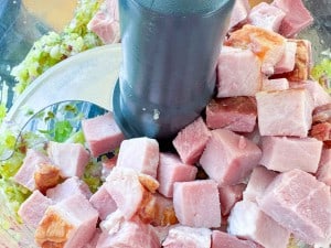 Cubed ham in a food processor bowl with chopped celery and onions.