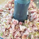 Chopped ham, pickles, and onions inside a food processor bowl, showing a mixed and finely diced texture.