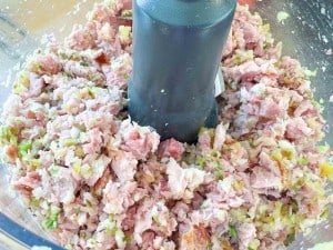 Chopped ham, pickles, and onions inside a food processor bowl, showing a mixed and finely diced texture.