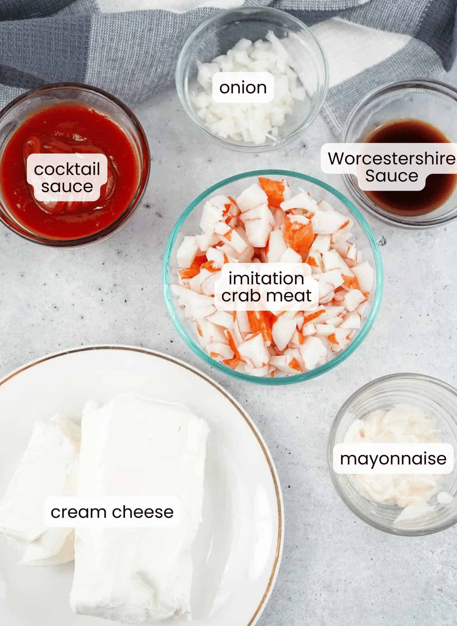 A top view of separate bowls containing cocktail sauce, chopped onion, Worcestershire sauce, imitation crab meat, cream cheese, and mayonnaise—perfect ingredients for a delicious Crab Dip with Cocktail Sauce.
