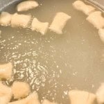Dough pieces boiling in cloudy water, likely being cooked to make gnocchi or dumplings.