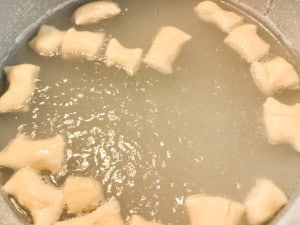 Dough pieces boiling in cloudy water, likely being cooked to make gnocchi or dumplings.
