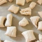 Small, unevenly cut pieces of raw dough are spread out on a silicone baking mat.