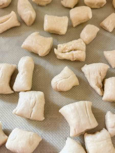 Small, unevenly cut pieces of raw dough are spread out on a silicone baking mat.