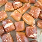 Bite-sized pretzel pieces with coarse salt sprinkled on top, arranged on a baking mat.