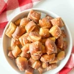 A white bowl filled with salted soft pretzel bites sits on a white surface next to a red and white checkered cloth.
