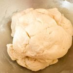 A ball of raw dough sits in a metal mixing bowl, ready to be kneaded or rolled out for baking.