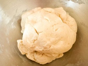A ball of raw dough sits in a metal mixing bowl, ready to be kneaded or rolled out for baking.
