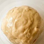A ball of unbaked dough sits in a white bowl, lightly coated with oil.