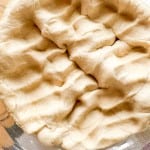 Unbaked, wrinkled pie crust dough pressed into a glass pie dish, ready for filling or baking.