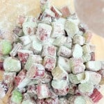 Chopped rhubarb pieces, perfect for a classic rhubarb pie, are coated in granulated sugar and flour and arranged in a pile on a light-colored surface.