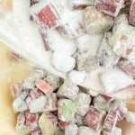 Chopped pieces of rhubarb, just right for a classic rhubarb pie, coated in granulated sugar on a sheet of parchment paper.