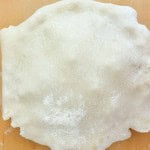 Unbaked pie crust laid over a pie dish on a wooden surface, with excess dough hanging over the edges, ready to be filled for a classic rhubarb pie.