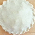 Unbaked classic rhubarb pie with crimped edges sits on a wooden surface, covered with a layer of raw dough.