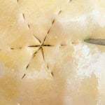 Close-up of an unbaked classic rhubarb pie crust, with star-shaped slits and a brush gently applying an egg wash.
