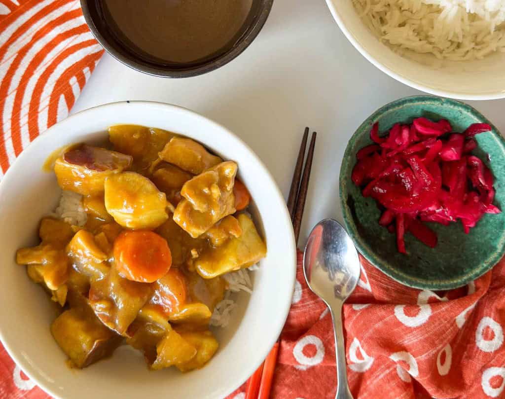 A bowl of chicken curry with rice, pickled cabbage, and a cup of broth.