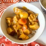 A white bowl filled with white rice topped with chicken curry featuring potatoes and carrots.