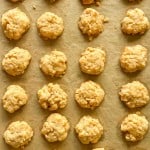 Rows of small, round, golden cheese crackers are arranged on a parchment-lined baking sheet.