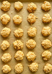 Rows of small, round, golden cheese crackers are arranged on a parchment-lined baking sheet.