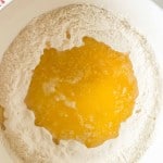 A white bowl contains flour with melted butter poured in the center, ready to be mixed for baking.