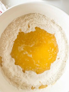 A white bowl contains flour with melted butter poured in the center, ready to be mixed for baking.
