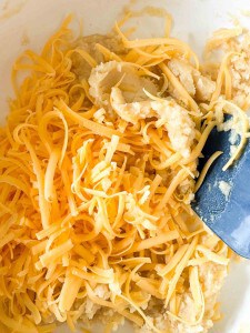 Shredded cheddar cheese and dough mixture in a bowl with a blue spatula.