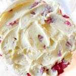 Close-up of a creamy mixture with visible pieces of strawberries, spread in a glass bowl.