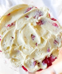 Close-up of a creamy mixture with visible pieces of strawberries, spread in a glass bowl.
