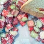 Close-up of chopped rhubarb pieces coated in sugar, being stirred with a wooden spoon.